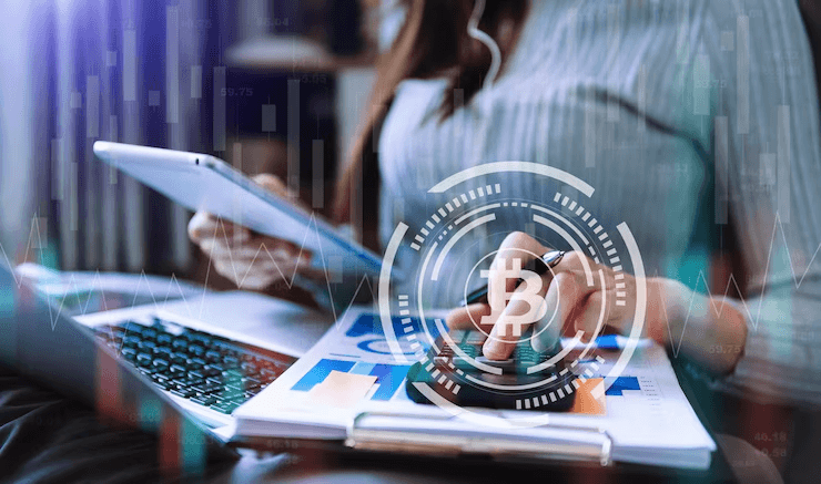 Person working on laptop and tablet with a calculator, overlaid with Bitcoin icon and financial charts, representing cryptocurrency business or analysis.